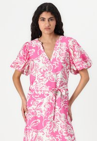 Rochie cu imprimeu floral în roz și alb, având un decolteu adânc în V, mâneci scurte tip bufant și un belciug legat la talie. Material ușor, cu un finisaj texturat.