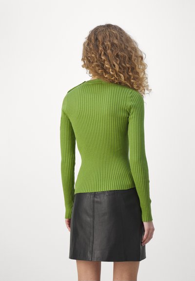 Rippstrickpullover mit langen Ärmeln in leuchtendem Grün, figurbetont geschnitten. Kombiniert mit einem schwarzen Leder-Minirock, glatte Textur und minimalistisches Design.