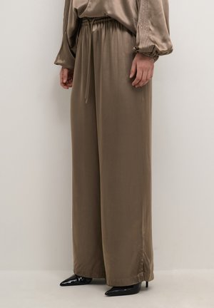 Loose-fitting taupe pants with elastic waistband and drawstring, worn with black pointed-toe heeled shoes and matching taupe blouse sleeves visible.