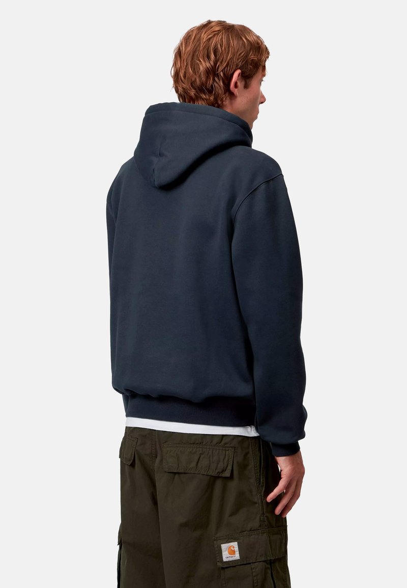 Felpa con cappuccio blu navy, dal taglio rilassato, con polsini e vita a costine; indossata con pantaloni cargo oliva con tasche laterali.