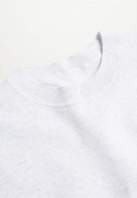 Gros plan d'un pull blanc à col rond montrant une texture fine en maille et un col côtelé sur un fond clair.