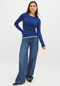Blaues Langarmhemd mit weißen Akzenten, kombiniert mit weit geschnittenen Jeans. Das Hemd ist figurschmeichelnd und aus einem dehnbaren Stoff gefertigt.