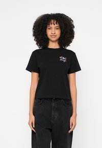 T-shirt preta de algodão com um corte descontraído, apresentando bordado floral colorido na área do peito esquerdo e mangas curtas.