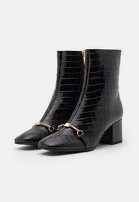 Botines negros de tobillo hechos de cuero sintético texturizado imitación cocodrilo, con punta afilada, un tacón bloque de altura media y un detalle de hardware en tono dorado.