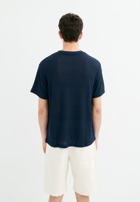 Camiseta de manga corta azul marino con textura acanalada, corte recto y cuello redondo, combinada con pantalones cortos de color claro.