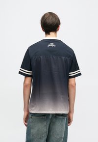 T-shirt με κοντά μανίκια σε ναυτικό μπλε χρώμα, με εφέ γραδίου (ombre), λευκές ρίγες στα μανίκια και διάτρητη υφή. Λογότυπο "JACKER" στη πλάτη.