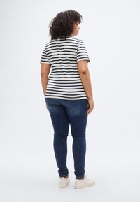 Κοντομάνικο ριγέ μπλουζάκι σε μπεζ και ναυτικό μπλε, συνδυασμένο με σκούρο μπλε τζιν στενής εφαρμογής και μπεζ αθλητικά παπούτσια. Εμφανίζεται από πίσω.