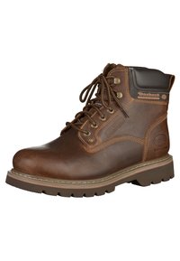 Bota de cuero marrón con cordones, con un collar acolchado, suela de goma y un detalle de logo sutil en el lateral. Construcción resistente con acabado texturizado.