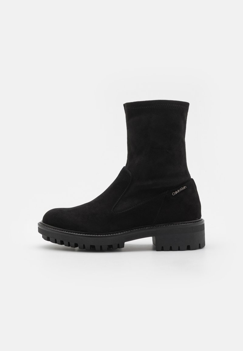 Bottes bottines en daim noir à finition lisse, bout rond, et semelle en caoutchouc texturée. Détail du logo sur le côté avec une tige de hauteur moyenne.