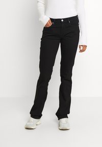 Jeans negros de mezclilla, con un corte clásico, diseño de cinco bolsillos, cierre frontal de botón y textura lisa. Llevados con una blusa blanca.