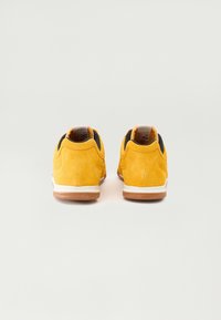 Yellow suede sneakers with black lining, white midsole, and brown rubber outsole. Features a rounded toe and padded collar.