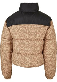 En pufferjakke med en svart toppseksjon og en beige bunnseksjon som har et intrikat brunt blomstermønster; den har høy krage og elastiske mansjetter.