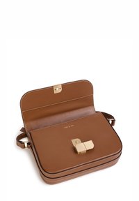 Brun korsärksväska i läder med guldfärgad spänne delvis öppen, synliga sömmar och justerbar rem på vit bakgrund.