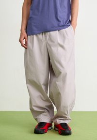 Lys grå løse bukser med elastisk talje og snøre, parret med sorte og røde sneakers, iført en blå t-shirt.