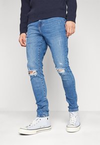 Jeans entallados de color azul claro con desgastes en las rodillas, combinados con zapatillas altas blancas. La tela es de mezclilla, con una textura suave.