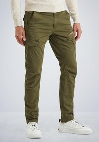Olivno zeleni cargo hlače z več žepi, zoženim krojem in gladkim, teksturiranim materialom. V kombinaciji z belimi športnimi čevlji.