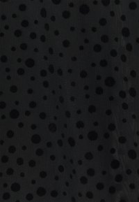 Tissu en maille noire avec des pois en velours de tailles variées espacés uniformément, créant un motif texturé.