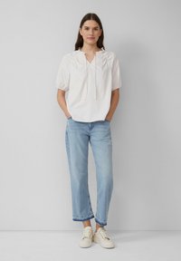 Biała koszula w paski z krótkim rękawem, dekoltem w serek i detalem w postaci wiązania, połączona z jasnoniebieskimi spodniami o prostych nogawkach oraz kremowymi trampkami.