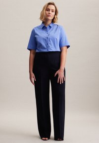 Camicia azzurro chiaro con bottoni e maniche corte, abbinata a pantaloni neri a vita alta. Tessuto liscio e design sartoriale; senza fantasie.