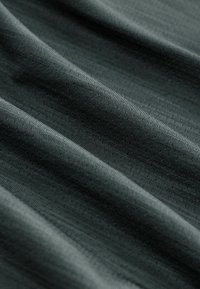 Tejido verde oscuro con una superficie lisa y ligeramente texturada, que presenta líneas horizontales sutiles y pequeñas perforaciones en toda su extensión.