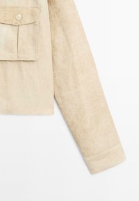 Beige Leinenhemd mit langen Ärmeln, Brusttasche und geknöpften Ärmeln, aus strukturiertem Stoff und mit einem lockeren Schnitt.