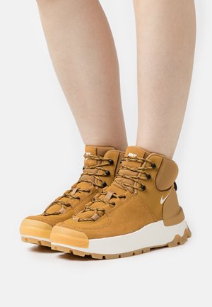 Baskets montantes marron en suede texturé, avec semelle en caoutchouc et accents noirs. Comprend un système de laçage et un col rembourré pour le soutien.