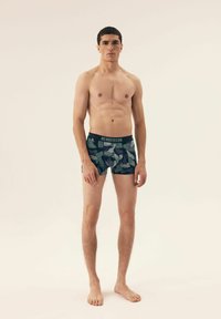 Bokserki z ciemnoniebieskim tłem z zielonym wzorem liści. Wykonane z miękkiego materiału z kontrastującym czarnym pasem wygodnym z napisem "HENDERSON".