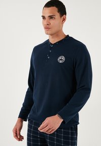 Polo din bumbac cu maneci lungi de culoare bleumarin, cu patru nasturi și o plăcuță cu logo rotund. Textura moale, croială lejeră și detaliu contrastant la gulerul interior.