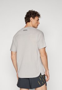 Light gray athletic t-shirt with short sleeves, textured back panel, and a subtle logo on the neckline. Smooth fabric and relaxed fit.