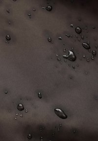 Des gouttes d'eau perlent sur une surface de tissu sombre, lisse et imperméable.