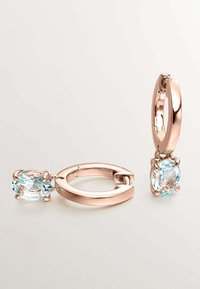 Pendientes de aro en oro rosa con un acabado texturizado, que presentan dos piedras ovaladas de color azul claro suspendidas en engastes de garra.