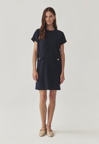Robe courte navy à manches courtes avec une coupe décontractée, dotée de deux poches avant avec des accents dorés. Tissu doux avec une texture lisse.