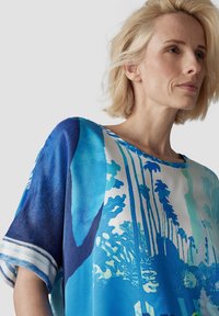 Lässig geschnittene, kurzärmelige Bluse in lebhaftem Blau mit Palmen-Print. Aus weichem Stoff gefertigt, mit einem entspannten Ausschnitt und gestreiftem Saum.