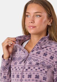 Fleecejack in lichtpaars met geometrische en sneeuwvlokpatronen. Bevat een ritssluiting en hoge kraag, zachte textuur en lange mouwen.