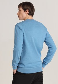 Pull-over léger en bleu clair fabriqué dans un tissu doux, avec des manches longues, un col rond et des poignets et un ourlet côtelés.