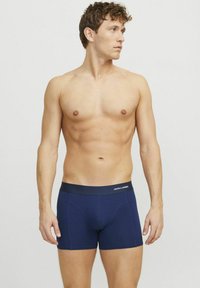 Navy blue cotton boxer briefs with a dark waistband featuring "JACK & JONES" logo. Smooth texture, fitted design, mid-thigh length.