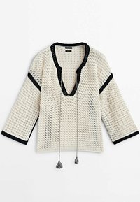 Top en crochet crème avec finition noire, décolleté en V, manches trois-quarts et détails de franges. Motif texturé sur l'ensemble du tissu.