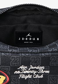 Juodas audinys viduje krepšio turi baltą logotipo etiketę su užrašu 'JORDAN' ir 'SINCE 1984'. Išsiuvinėtas tekstas sako 'Air Jordan no. Twenty Three Flight Club'.