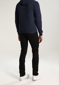 Námořnická mikina s kapucí, černé přiléhavé kalhoty a bílé tenisky. Materiály vypadají jako bavlna a denim s minimální texturou a designovými detaily.