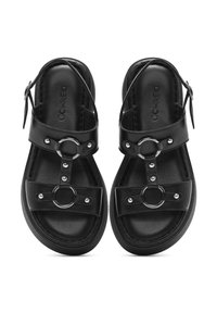 Sandali neri in pelle con un design minimalista, caratterizzati da dettagli metallici circolari e cinturini regolabili, suole flat e una texture liscia.