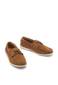 Brązowe zamszowe buty żeglarskie z okrągłym noskiem, kontrastowym przeszyciem i sznurowanym zapięciem. Posiadają jasnokolorową gumową podeszwę i brązowe akcenty.
