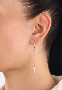 Pendientes de gota en oro rosado con una cadena delgada, que presentan acentos cilíndricos de diferentes longitudes, colgando de un pequeño aro.