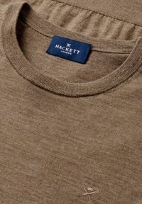 Bruine gebreide trui met een ronde hals, voorzien van een gestructureerde stof en een geborduurd logo in een contrasterende kleur nabij de zoom.
