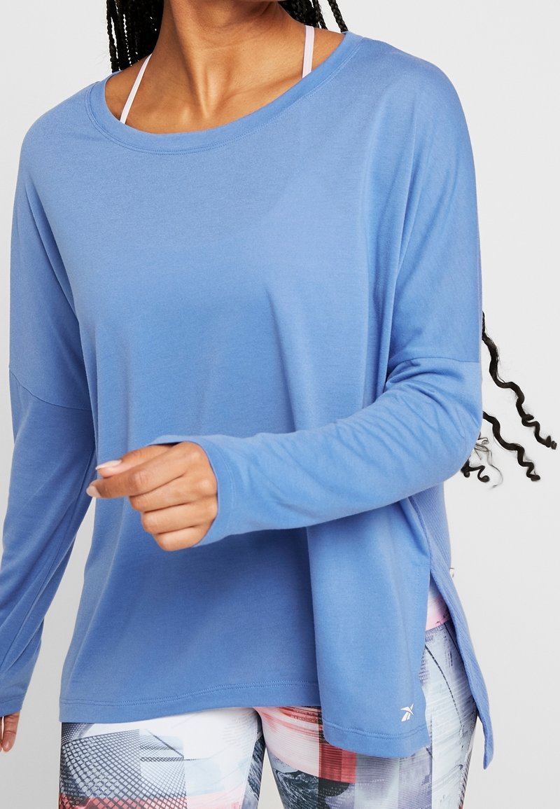 Blå långärmad sporttop med avslappnad passform, sidopartier, mjukt tyg och rundad halsringning, som matchas med mönstrade leggings.