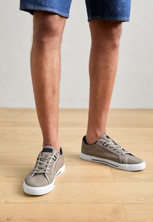 Szürke velúr sportcipők fehér gumitalppal, alacsony felsőrésszel és tengerészkék részletekkel. A fűzők és a perforált díszítések az oldalakon jól láthatók.