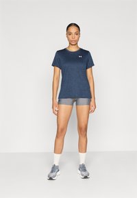 Μπλε ναυτικό αθλητικό πουκάμισο με κοντά μανίκια, σε συνδυασμό με γκρι αθλητικά σορτς. Ο μοντέλο φοράει γκρι παπούτσια για τρέξιμο με λευκές σόλες και κάλτσες μέσης.