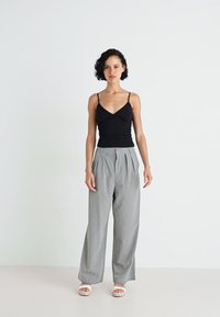 Débardeur noir ajusté avec des fines bretelles, associé à un pantalon large à rayures gris. Le mannequin se tient sur un fond neutre.