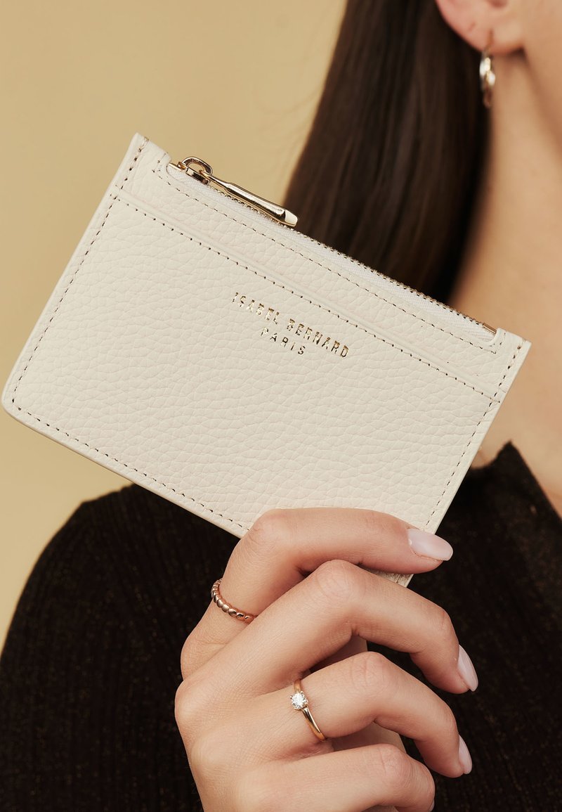 White leather cardholder with a textured finish, zippered closure, and embossed logo. Simple rectangular shape with accent stitching.