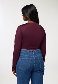 Długi rękaw bordowa bluzka o dopasowanej sylwetce, w połączeniu z niebieskimi dżinsami z wysokim stanem, z klasycznym pięciopocketowym krojem.
