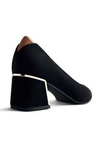 Zapato de tacón alto de ante negro con un tacón cuadrado que presenta un acento dorado en la base y un detalle marrón contrastante en la parte posterior.